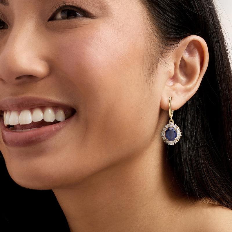 Worn gold drop earrings with blue sapphire and white topaz halo, dangling from hook