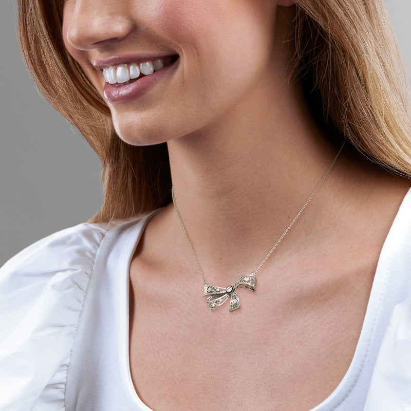 Diamond bow pendant necklace worn at the neckline with round center stone and ribbon detail