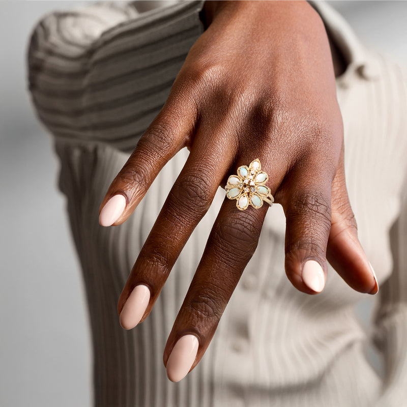 Opal and diamond cluster ring on hand, gold setting with flower-like openwork design