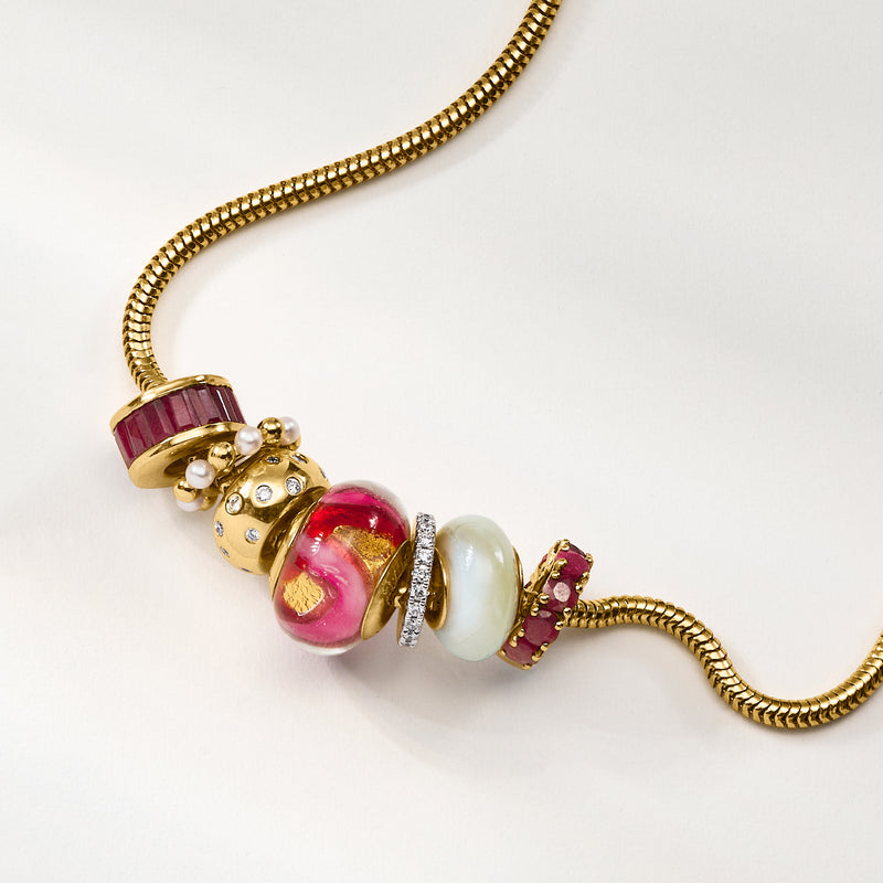 Close-up of gold charm bead with red baguette stone, pearls, and sparkling accents