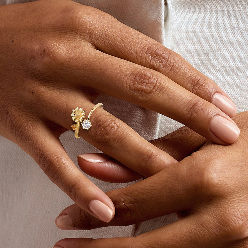 Gold daisy flower ring with round clear stone on finger, small orange side gem
