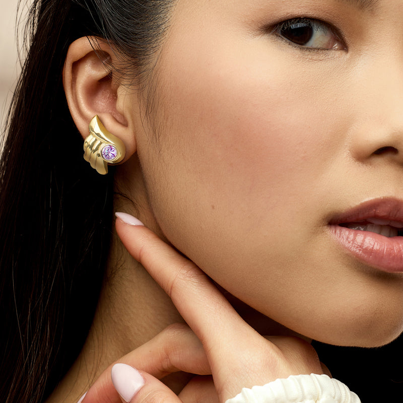 Gold tone clip/post earrings with purple round CZ stones on a model