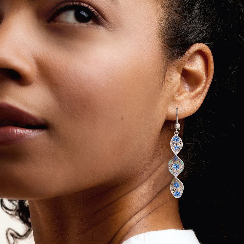 Sterling silver blue enamel floral twisted drop earrings on ear, three oval tiers