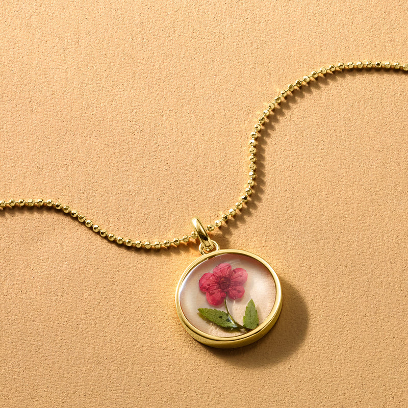 Gold-tone round locket pendant necklace with red flower behind glass