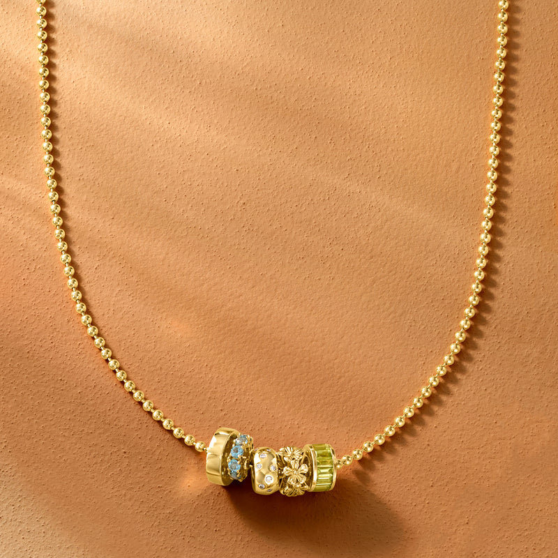 Gold bead charm with blue center and green accents on a slim gold chain necklace