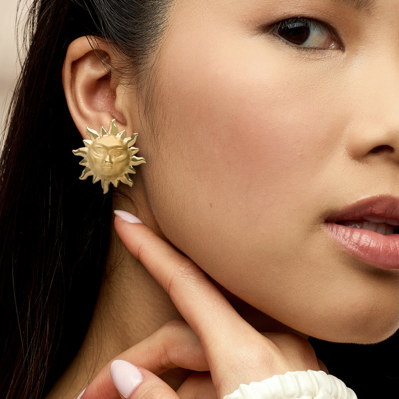 Yellow gold sun-face earrings on model ear, close-up of textured rays