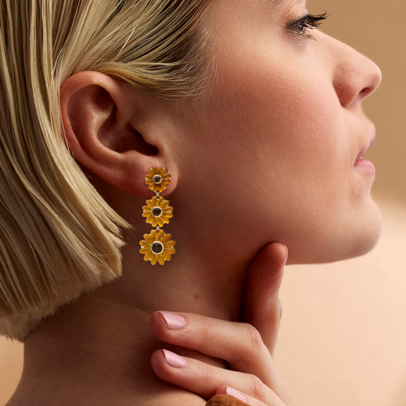 Sunflower drop earrings on ear: three gold blooms with dark centers