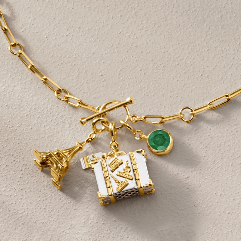 Gold-tone travel luggage charm with green gemstone accent and stacked city suitcase details