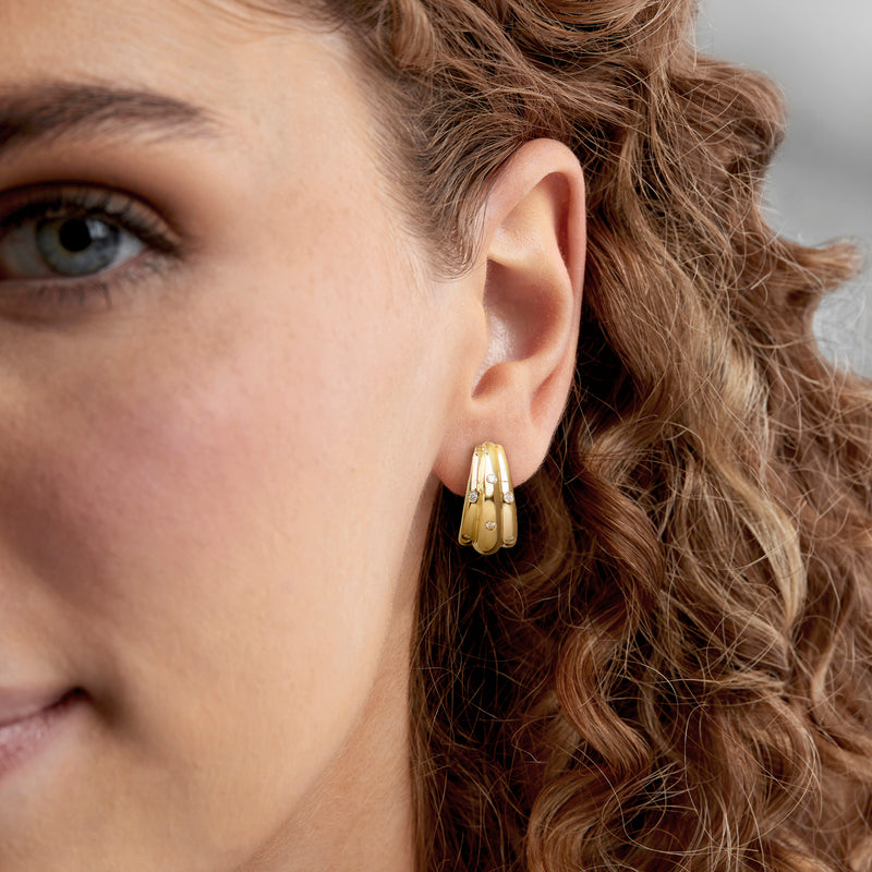 Curved 18kt yellow gold hoop earrings with round diamond accents worn on ear