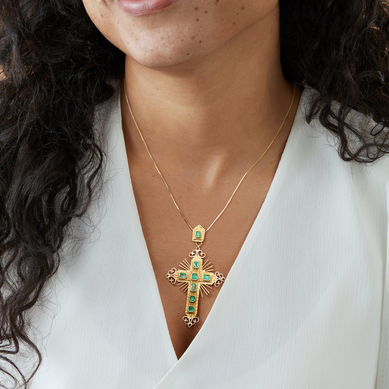 Gold cross pendant necklace with green gemstone center and dangling chain
