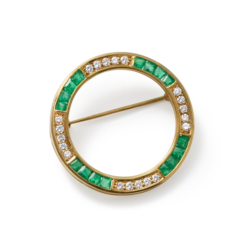 Round circle pin with green emerald channel border, white diamonds, and yellow gold clasp