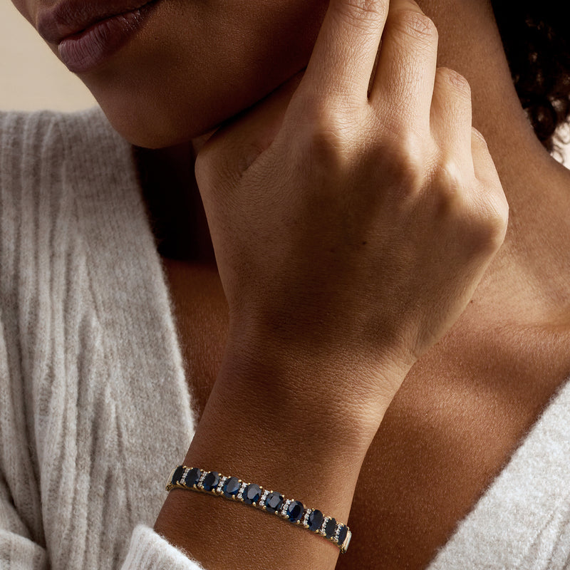 Sapphire and diamond tennis bracelet on wrist with blue oval stones in yellow gold