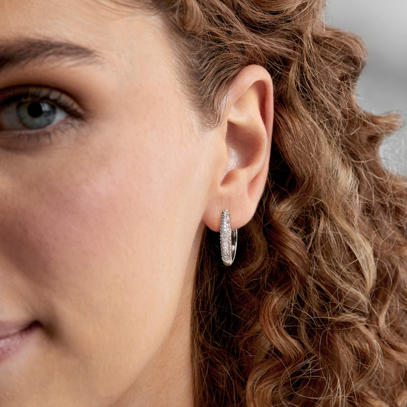 Diamond-studded oval hoop earrings in 14kt white gold worn on ear