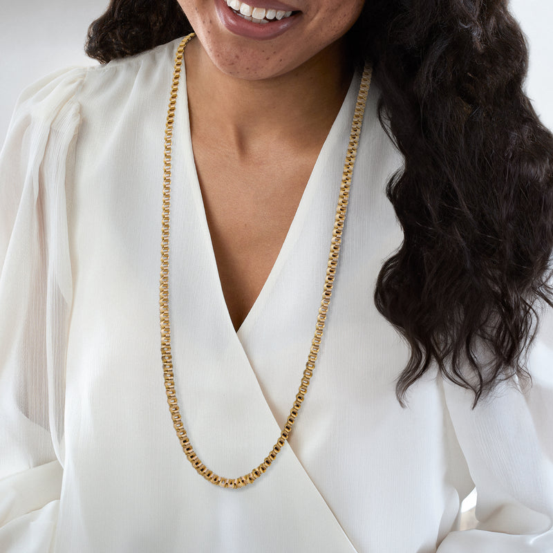Yellow gold fancy-link necklace worn over a white V-neck blouse