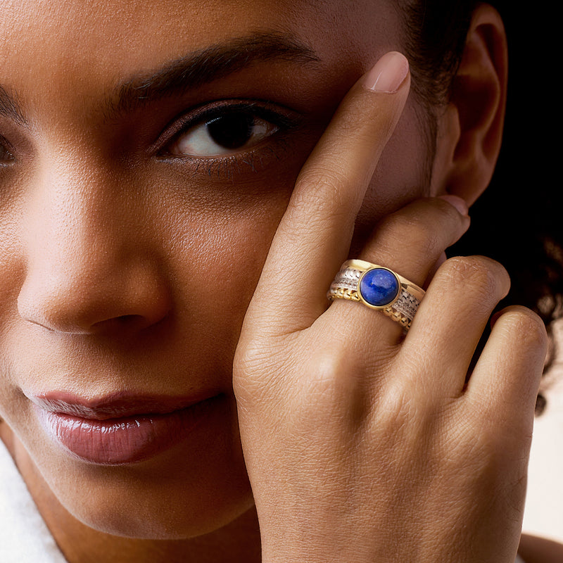 Round blue lapis cabochon ring on finger with gold and silver multi-row accents