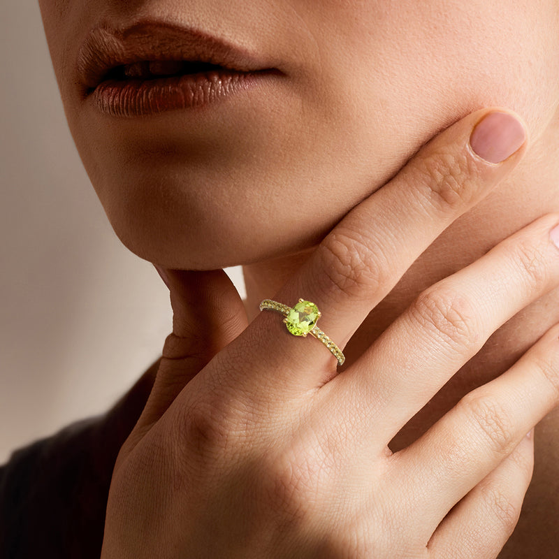 Gold-toned peridot ring on hand, oval green center with small round side stones