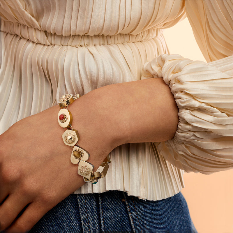 Yellow gold slide charm bracelet on wrist with oval and square gem charms