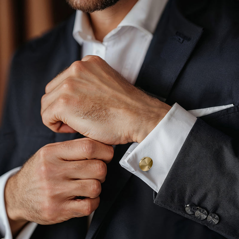 Yellow gold disc cuff links fastened on a dark suit shirt cuff, model wearing them.