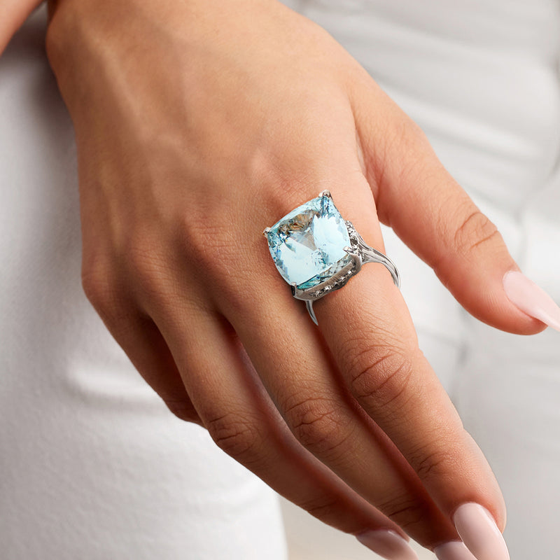 Aquamarine cocktail ring on hand, cushion stone with darkened halo and platinum band