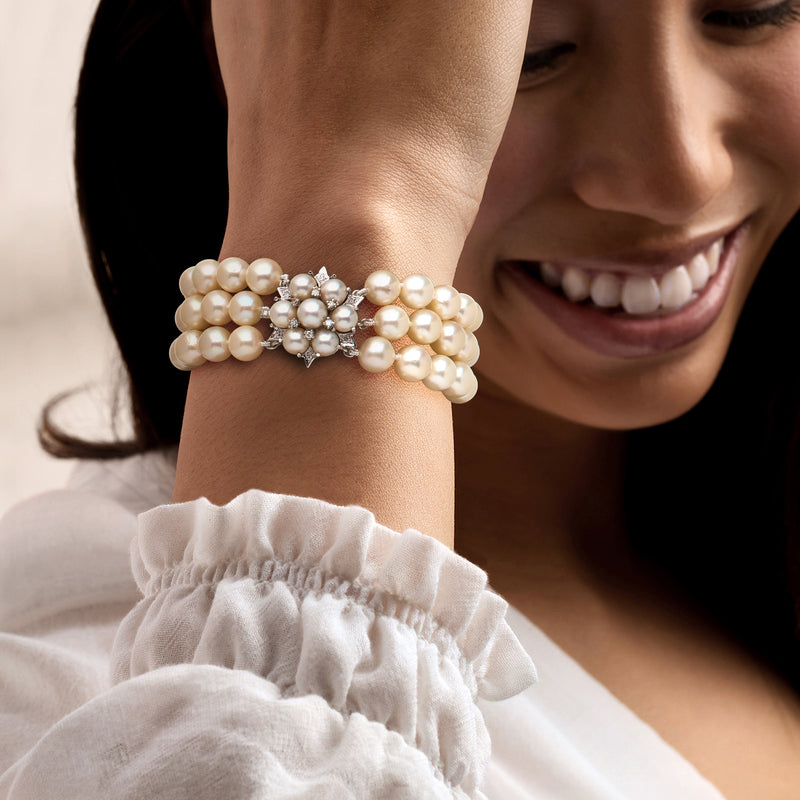 Cultured pearl three-row bracelet on wrist with diamond floral clasp detail.