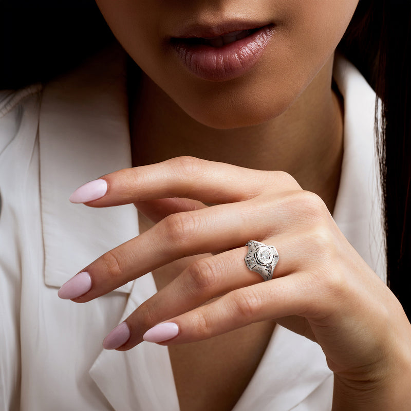 Diamond ring on finger with ornate 18kt white gold setting and bezel-set center stone