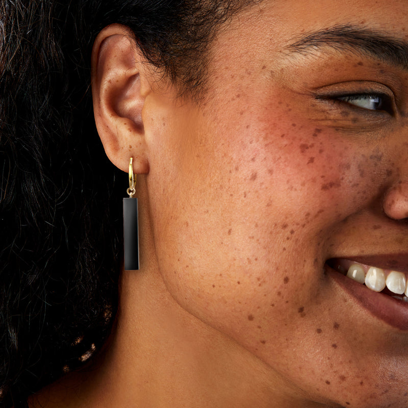 Gold onyx bar drop earrings with leverbacks, black rectangle worn on ear.