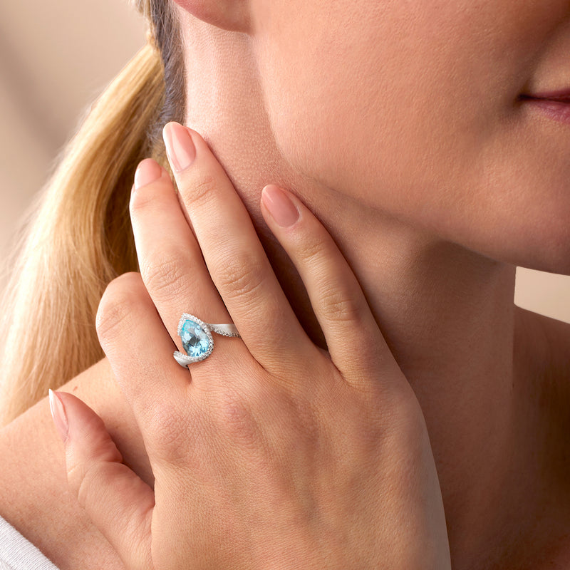 Light blue gemstone ring on finger with white gold band and diamond halo