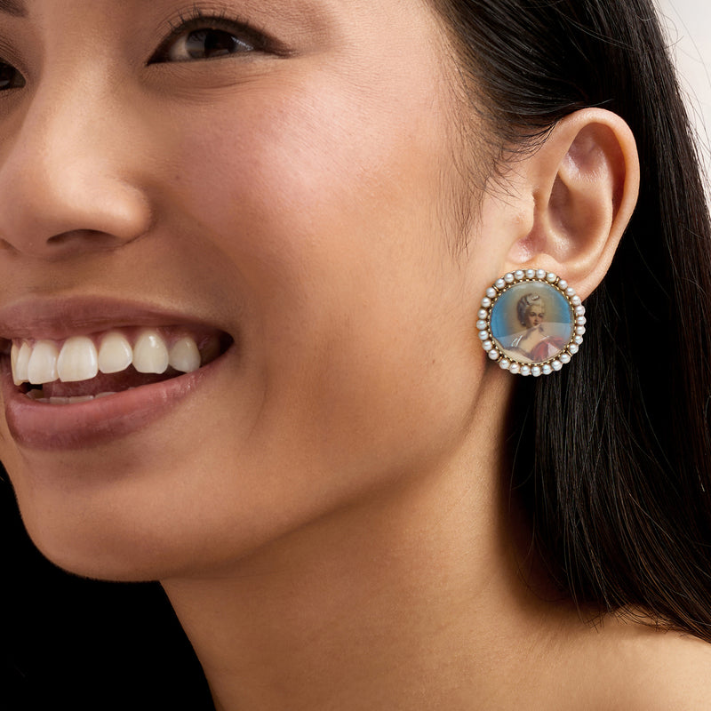 Cultured pearl-framed oval portrait earrings on model, blue enamel background