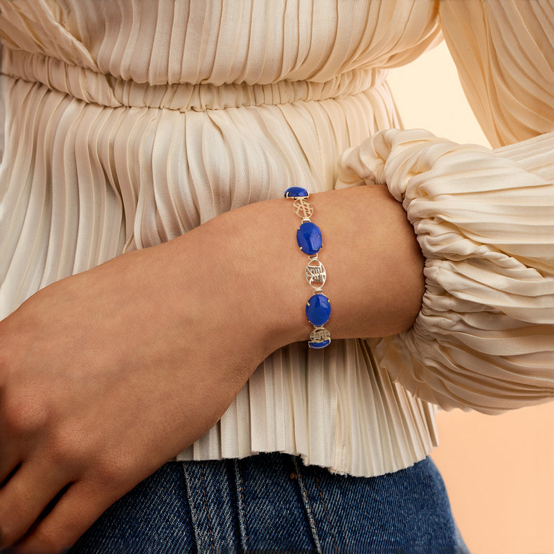 Blue lapis oval cabochon bracelet on wrist in 14kt yellow gold with engraved links