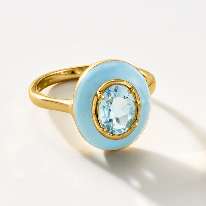 Gold ring with sky-blue oval gemstone framed by round blue enamel disc.