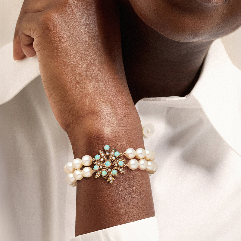 Two-strand cultured pearl bracelet on wrist with blue opal floral detail and gold setting
