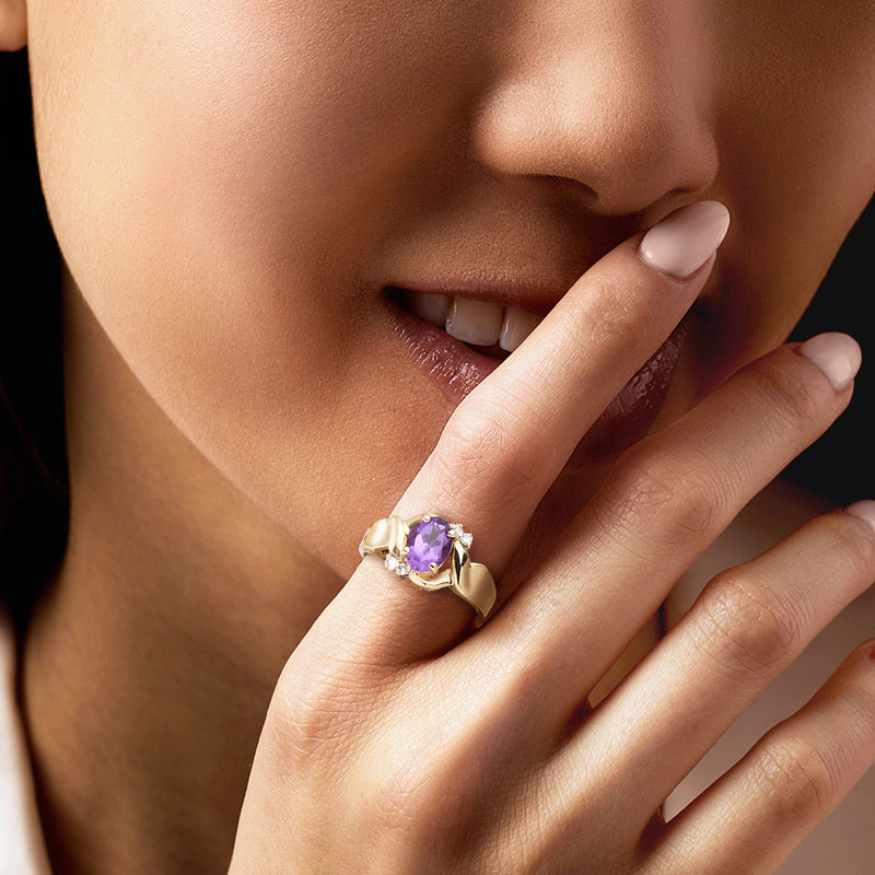 Amethyst ring on finger: 10kt yellow gold with oval purple gemstone and diamond band