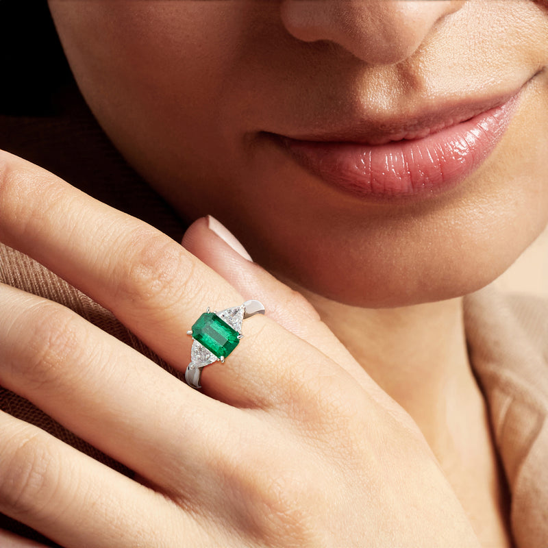 Emerald square ring on hand with platinum band and small diamond halo