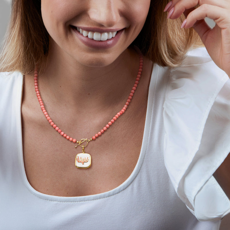 Gold coral reef charm pendant on red beaded necklace worn with white top