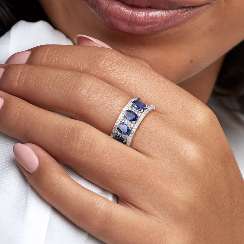 Blue sapphire and diamond ring worn on hand, oval stones set in white metal