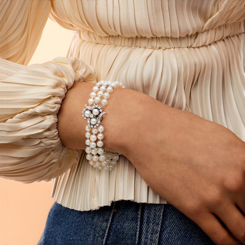 Three-row cultured pearl bracelet on wrist with jeweled clasp and round white pearls