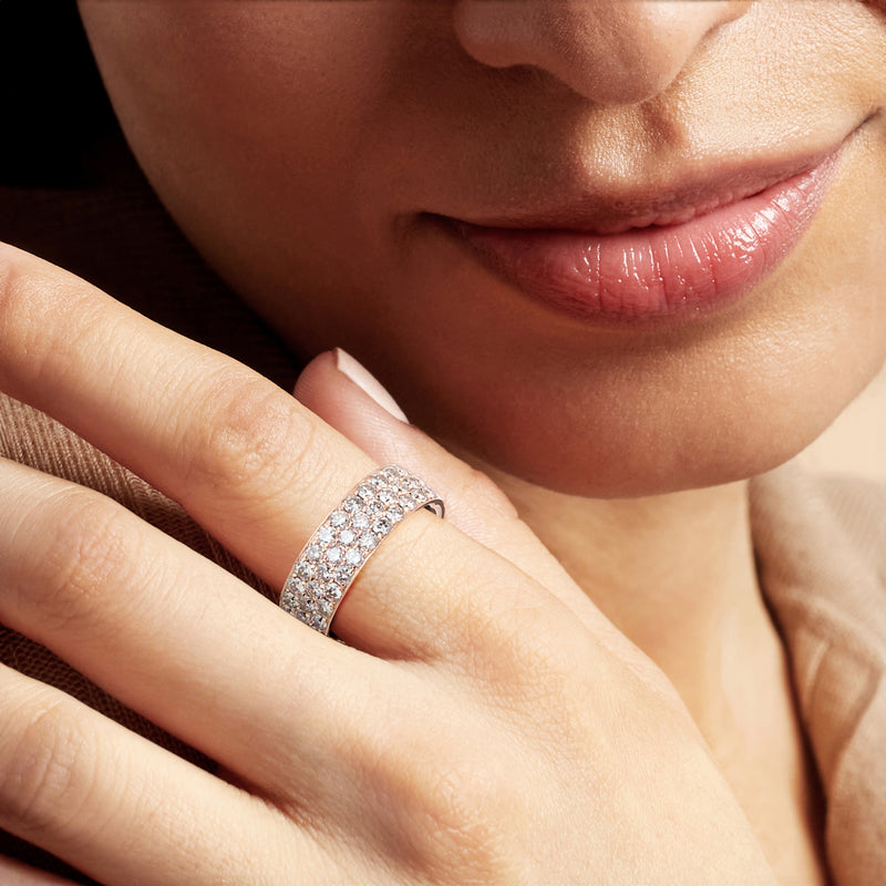 Rose gold diamond band ring with small round stones on finger, close-up.