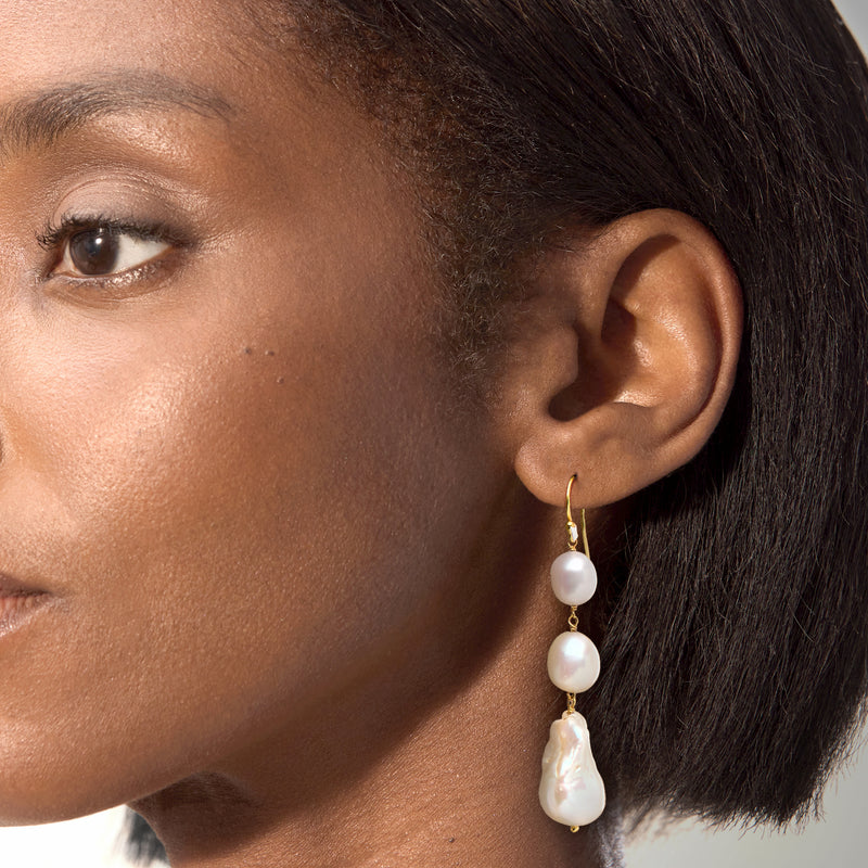 Model wearing gold-tone drop earrings with three white cultured pearls.
