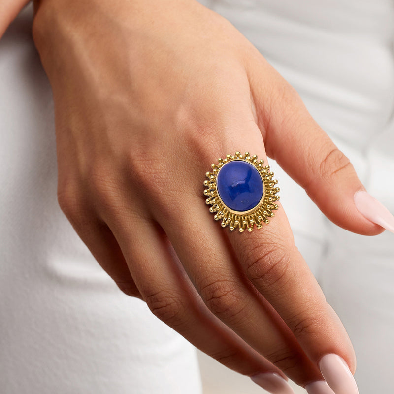 Lapis cabochon ring on hand with oval blue stone set in gold beaded halo