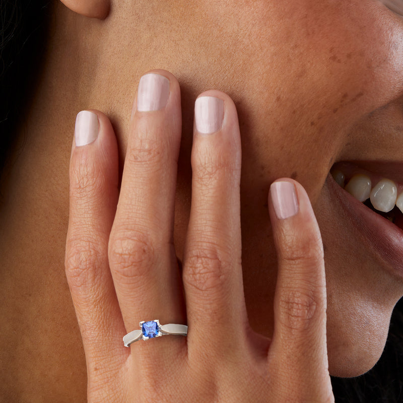 Sapphire ring on finger with square-cut blue stone and four-prong white metal band