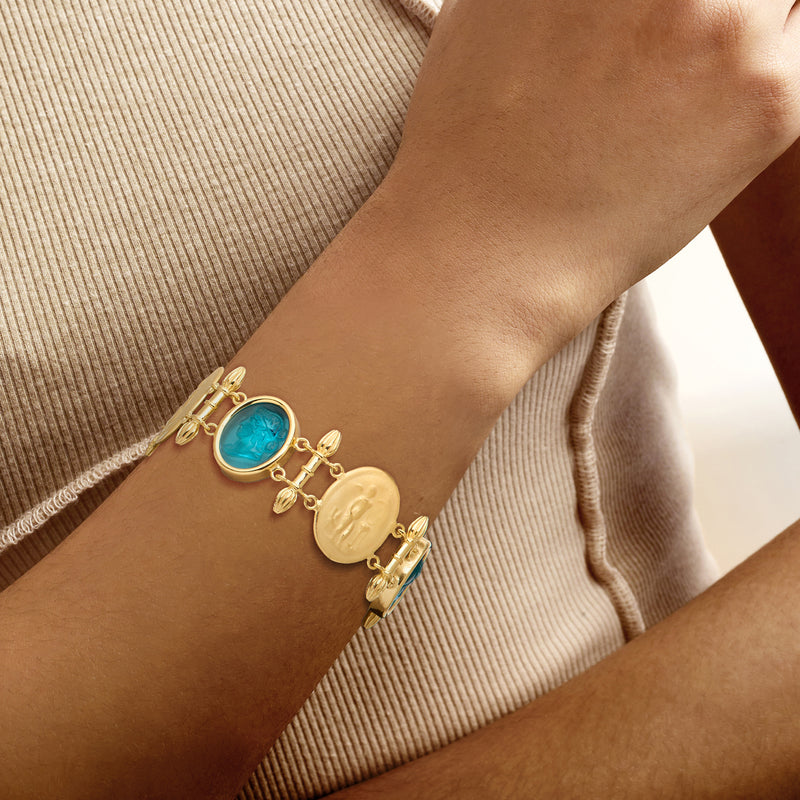 Gold-tone bracelet on wrist with blue oval glass stations and oval medallion charms
