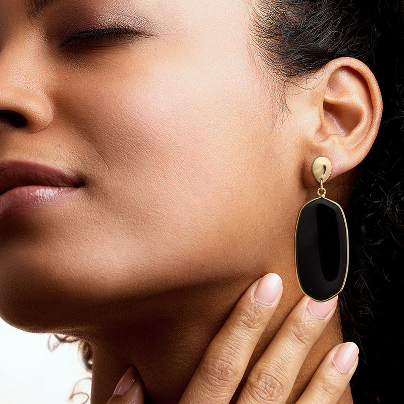 Gold-tone drop earring with black oval simulated onyx, close-up on ear