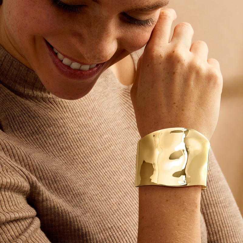 Wide yellow gold-plated hammered bangle bracelet worn on wrist