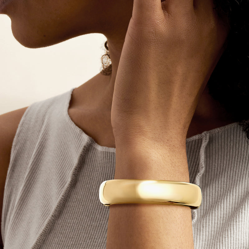 Yellow gold-plated rounded bangle bracelet worn on wrist, smooth cuff