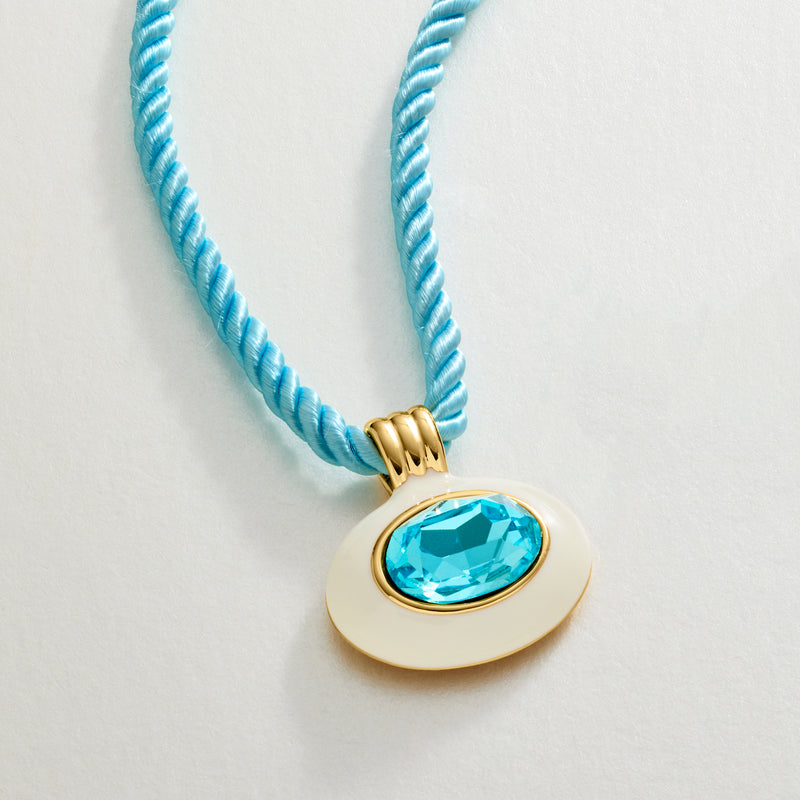 Gold-plated oval pendant with white enamel and bright blue simulated topaz on blue cord
