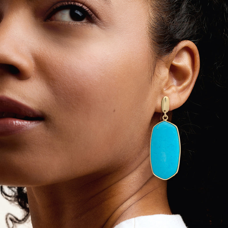 Gold-plated oval turquoise drop earrings, worn on model ear