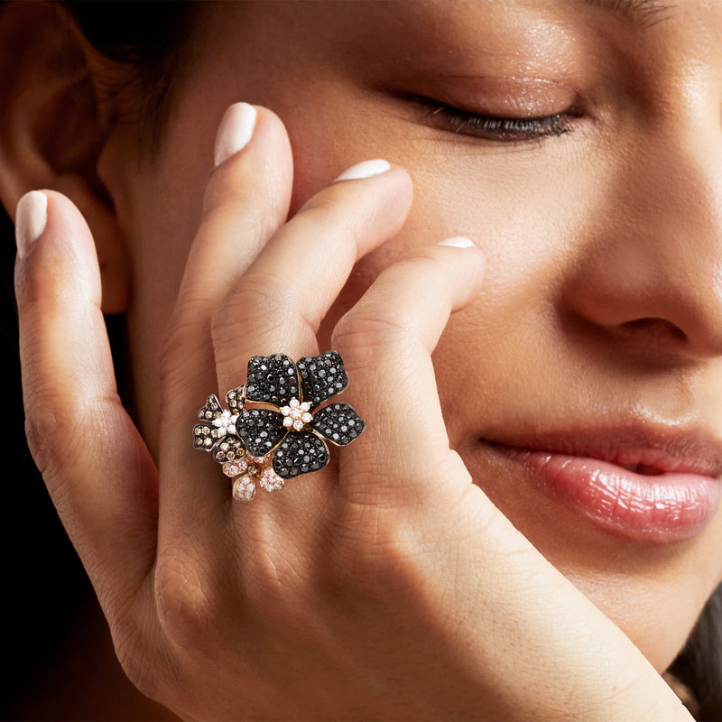 Diamond flower ring on finger in tri-colored 14kt gold, black and white sparkle.