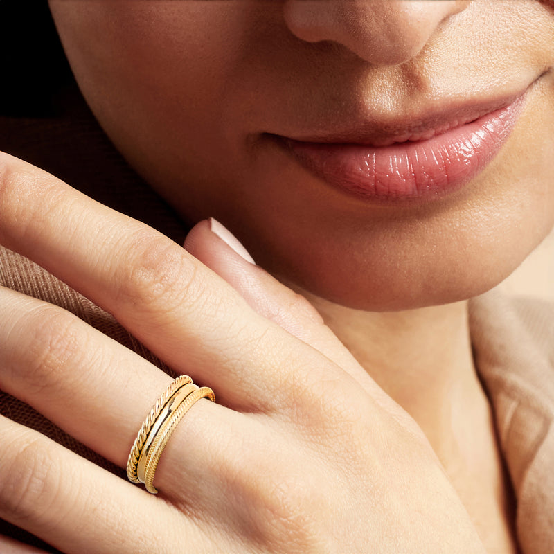 Three stackable gold-tone rings on a finger: braided rope texture and smooth band.