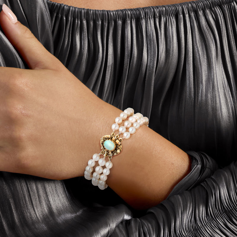 Three-row pearl bracelet on wrist with blue-green opal centerpiece in gold