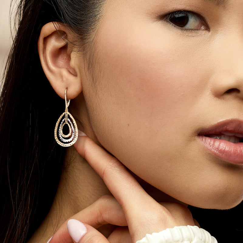 Two-tone gold teardrop earrings with concentric rings, worn on model’s ear